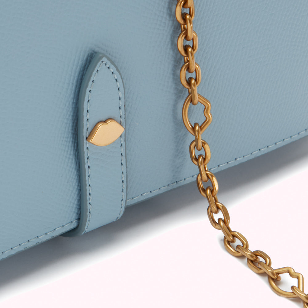 Close-up of a light blue leather wallet with a gold chain and lip-shaped detail.
