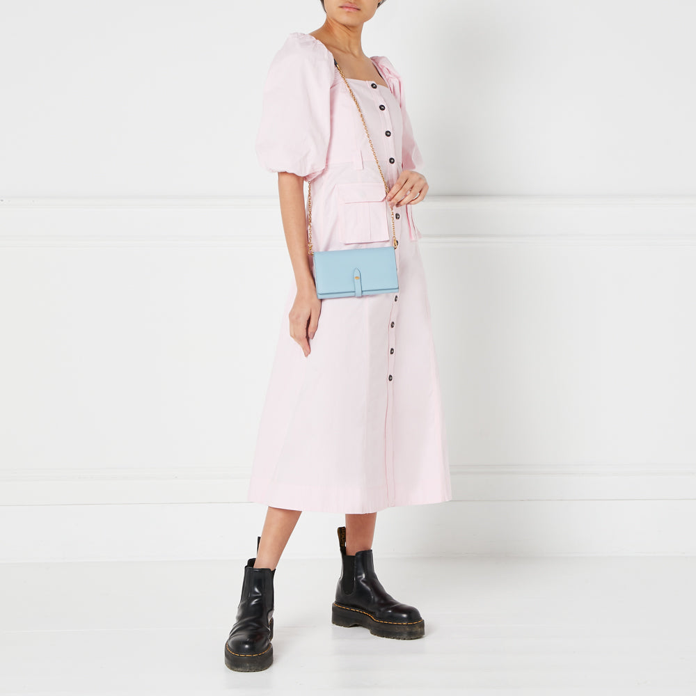 A woman in a pink dress and black boots carries a light blue crossbody wallet on a gold chain.