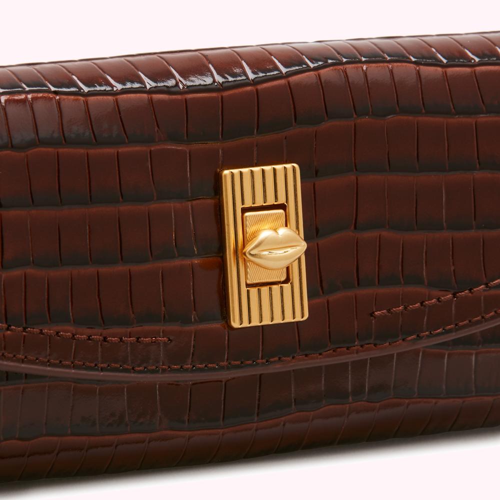 Close-up of a dark brown crocodile-embossed leather wallet with a gold lip-shaped clasp.

