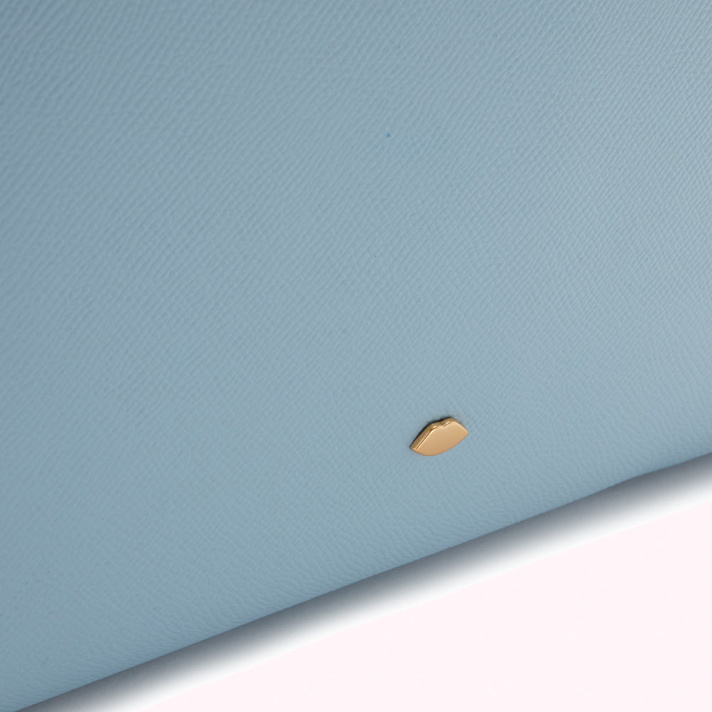 Close-up of a light blue textured leather surface with a small gold lip-shaped logo.
