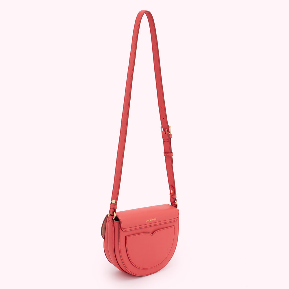 Coral-coloured half-moon crossbody bag with gold hardware and long strap.
