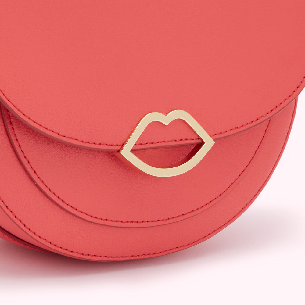 Close-up of a coral-coloured leather handbag with a gold lip-shaped clasp.
