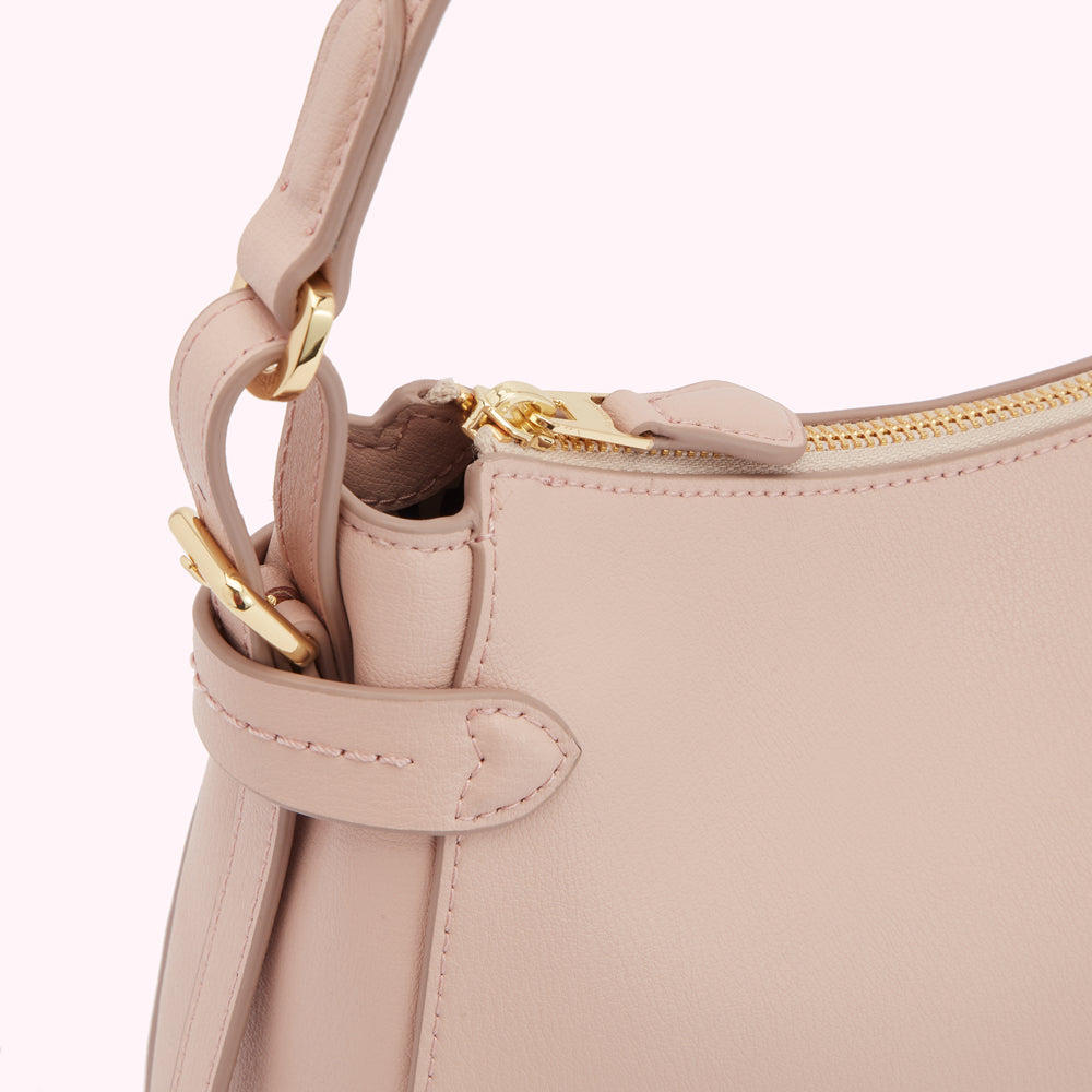 Close-up of a blush pink leather handbag with gold zipper and hardware.
