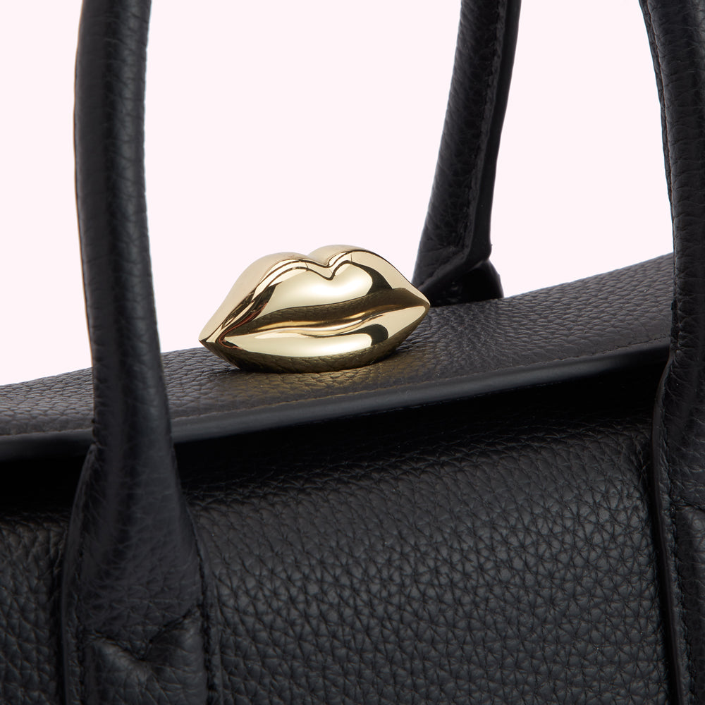 Close-up of a black leather handbag with a gold lip-shaped clasp.
