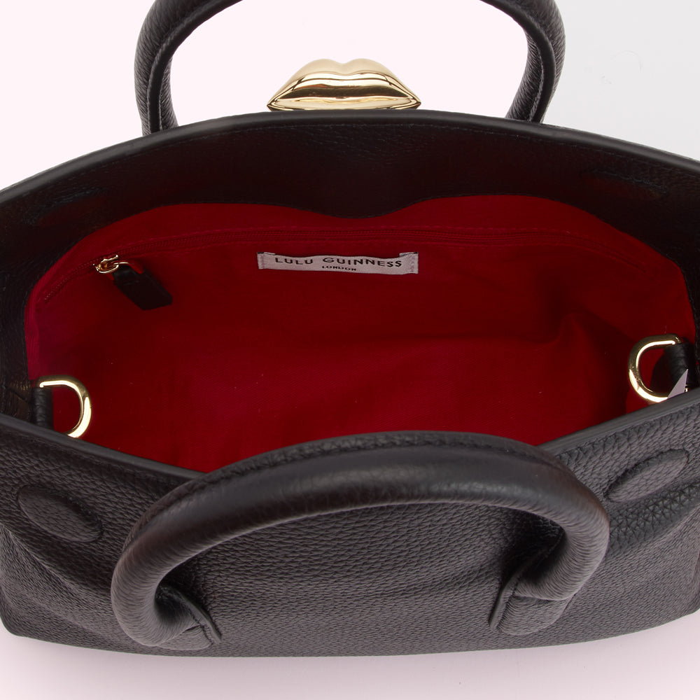 Interior view of a black Lulu Guinness London handbag with a red lining and gold heart-shaped clasp.