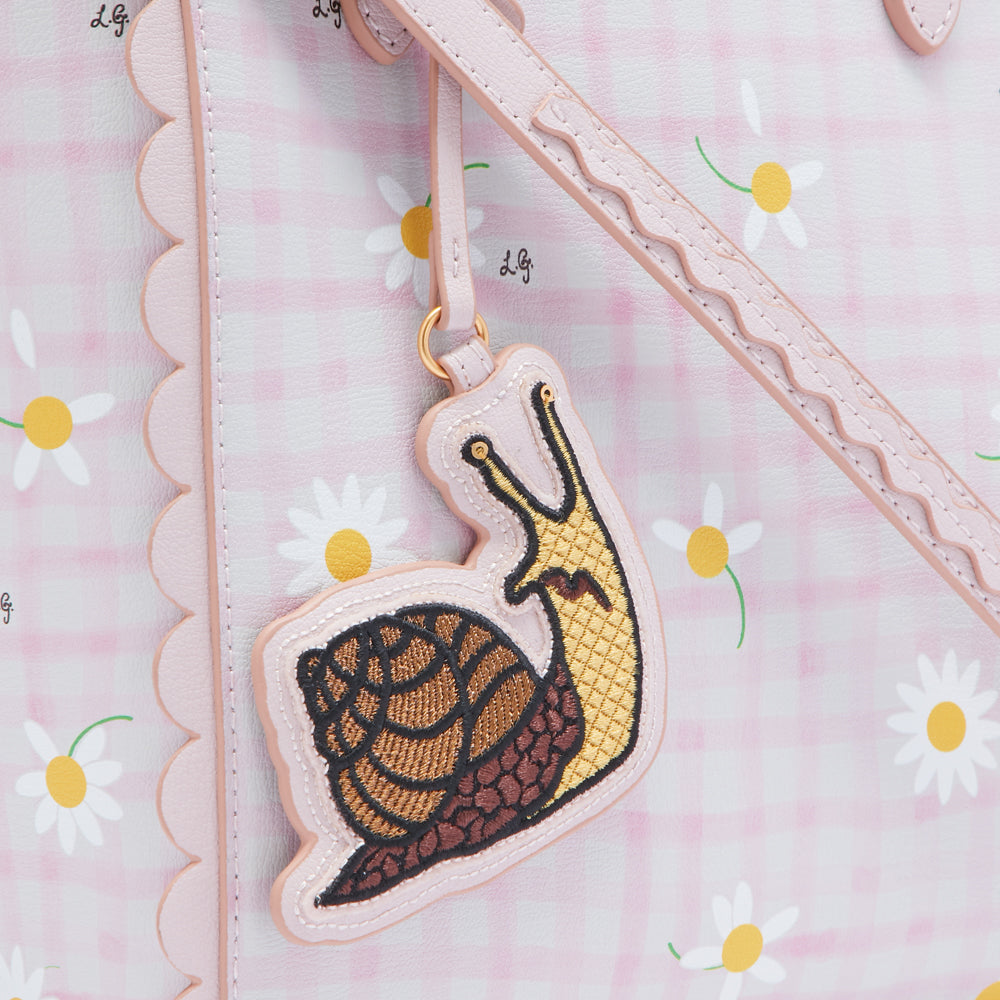 Close-up of a pink handbag with a scalloped edge, adorned with a daisy print and a snail-shaped charm.