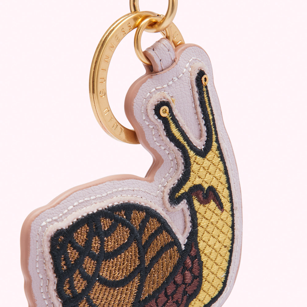 Close-up of a pink and gold snail-shaped keyring with embroidered details.