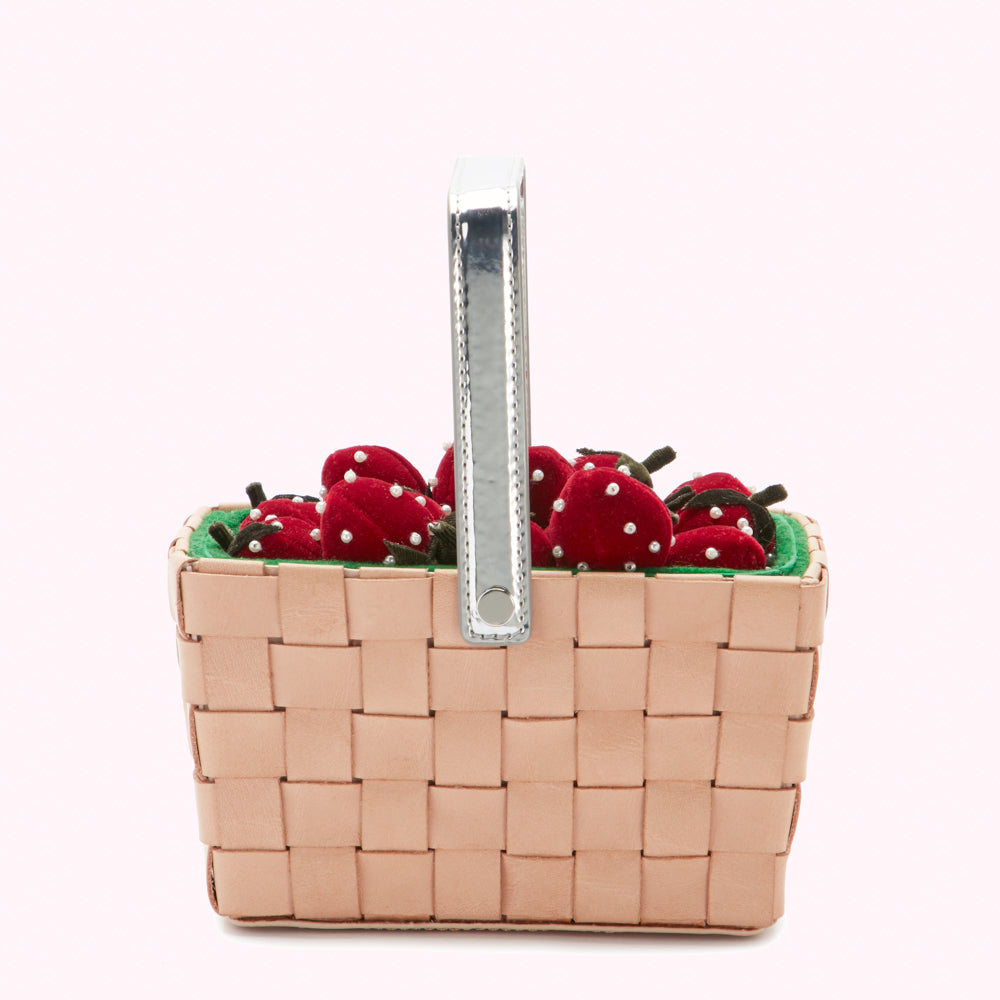 A beige woven basket handbag with a silver handle filled with red velvet strawberries.