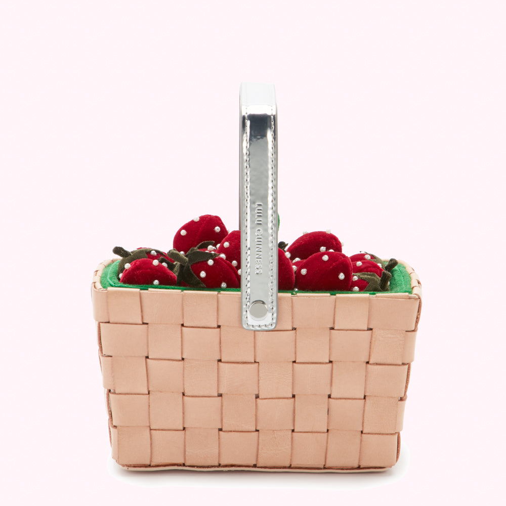 Pink woven basket handbag with a silver handle filled with red velvet strawberries.