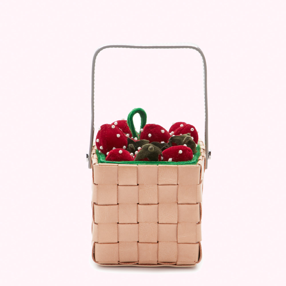 A light beige woven basket with a silver handle filled with red velvet strawberries and green velvet leaves.