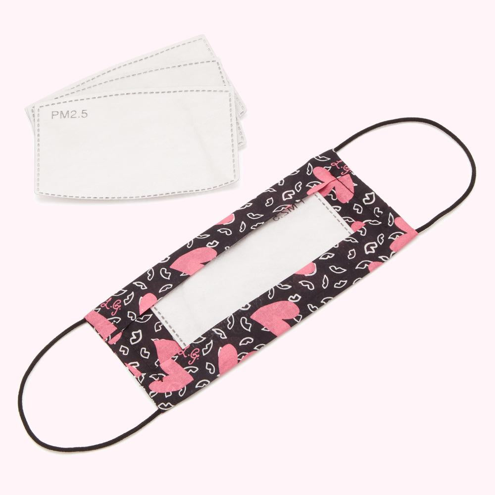 Black face mask with pink lips and hearts pattern, and clear window showing replaceable PM2.5 filters.
