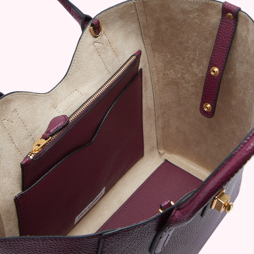 Inside view of a burgundy pebbled leather tote bag with a beige interior, showing a zippered pocket.
