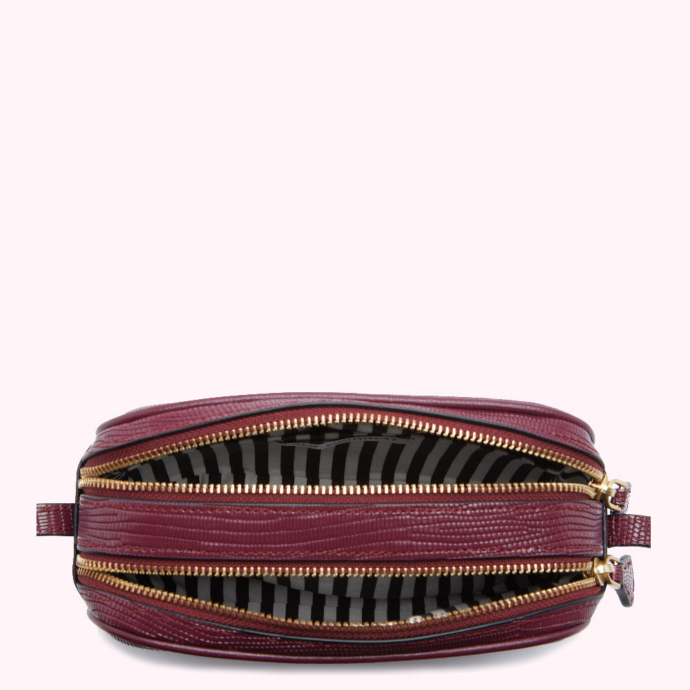 Burgundy crossbody bag open to reveal its two compartments and striped lining.
