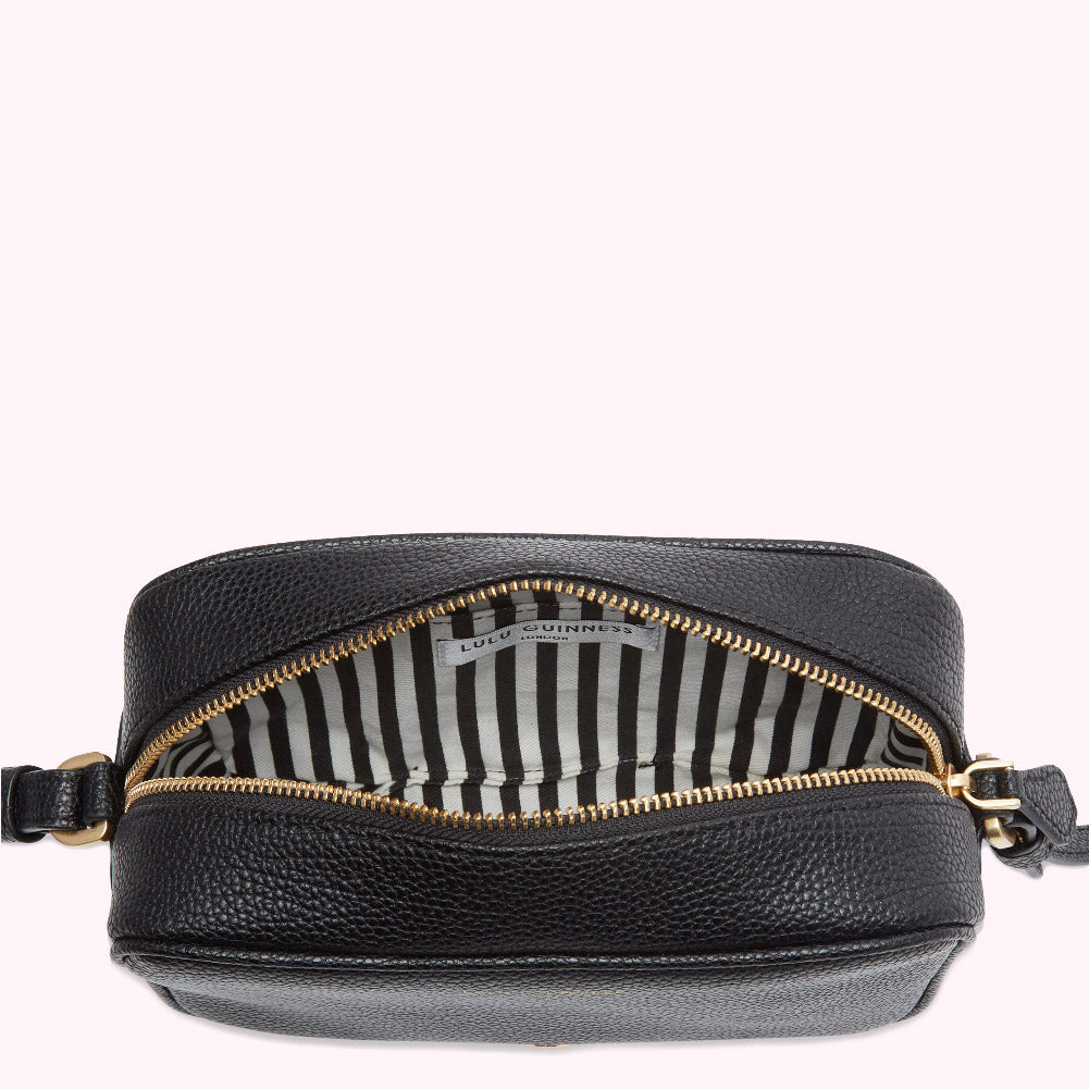 Black Lulu Guinness crossbody bag open to reveal black and white striped interior.
