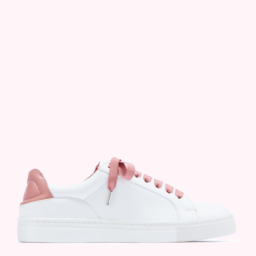 White leather sneaker with dusty rose accents and laces on a pink background.
