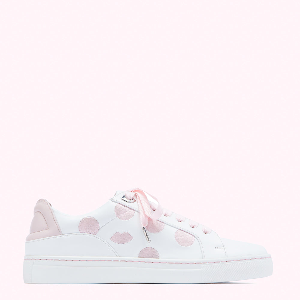 White leather sneakers with pink polka dots and lips, on a pink background.