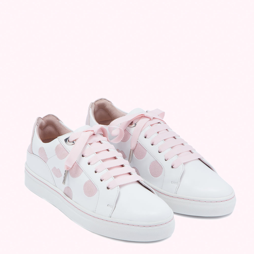 Pair of white leather sneakers with pink polka dots and pink laces against a pink background.