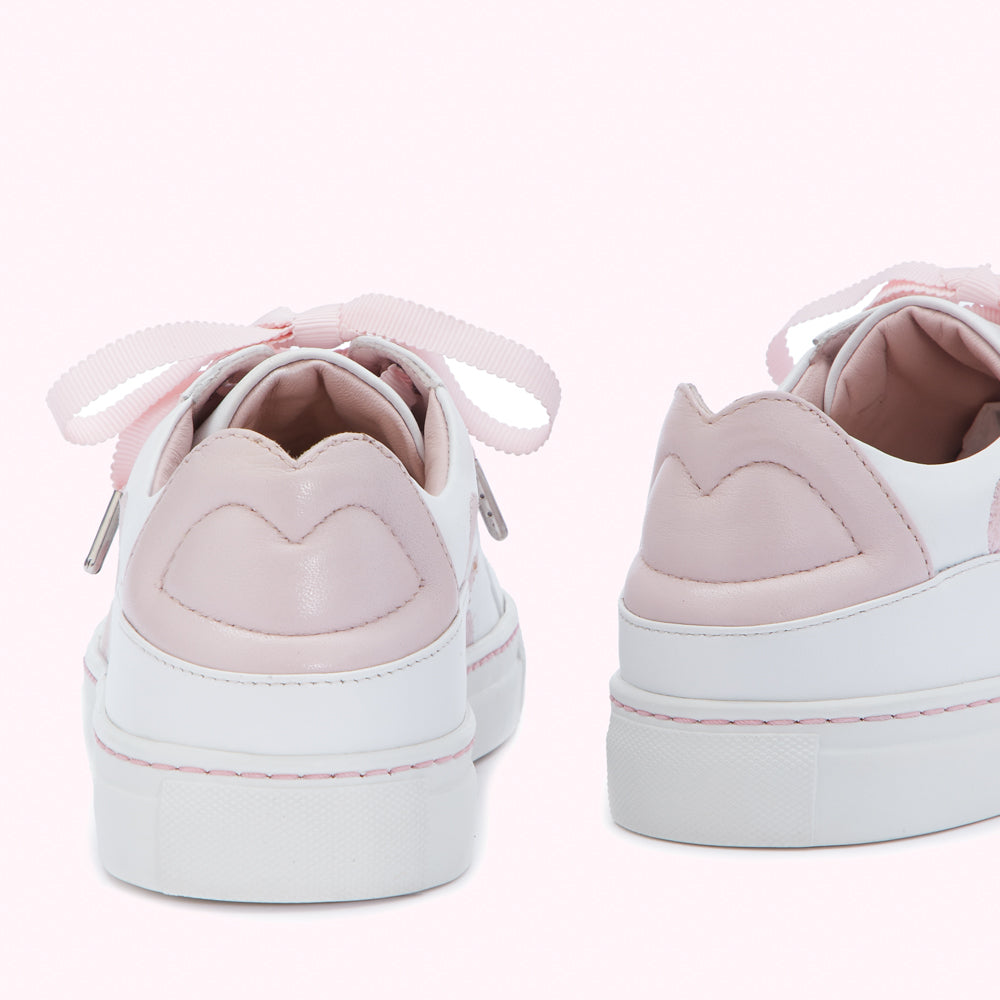 Pair of white and pink sneakers with pink ribbon laces, viewed from behind against a pink background.
