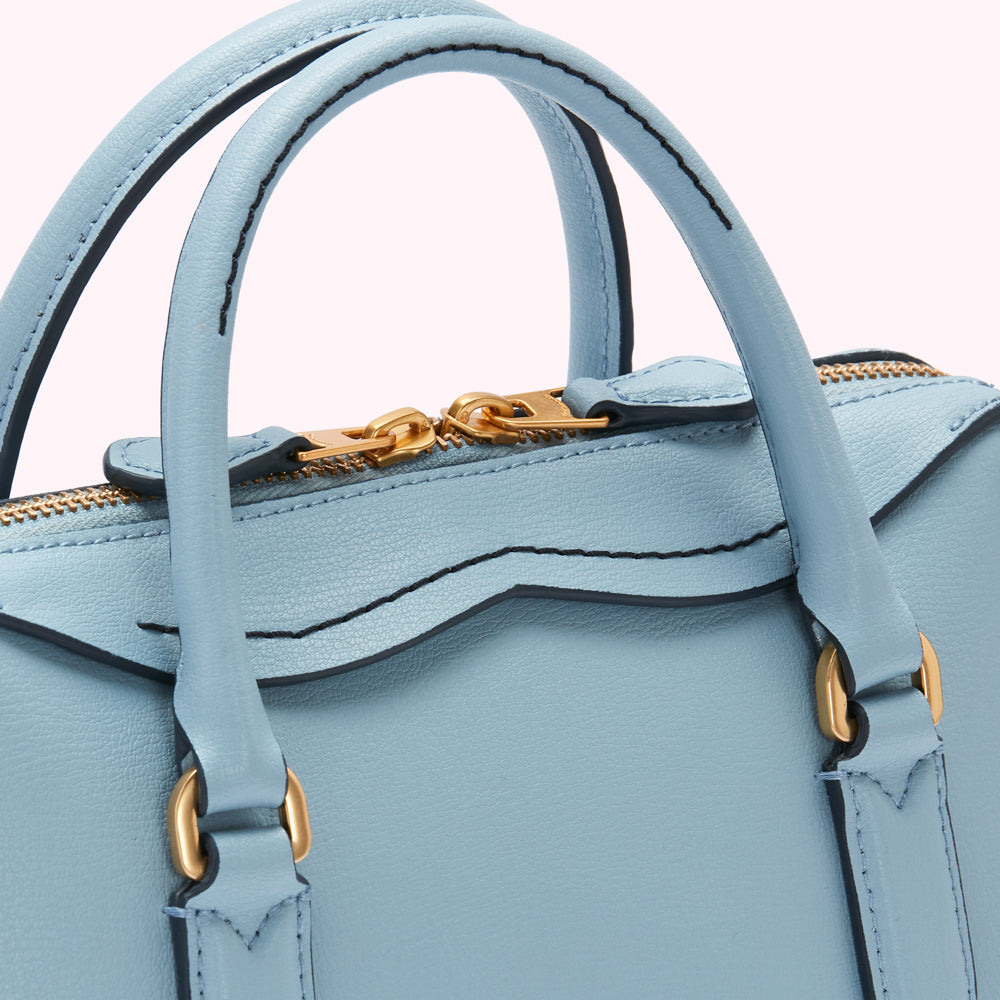 Close-up of a light blue leather handbag with gold-toned hardware and a top zip closure.
