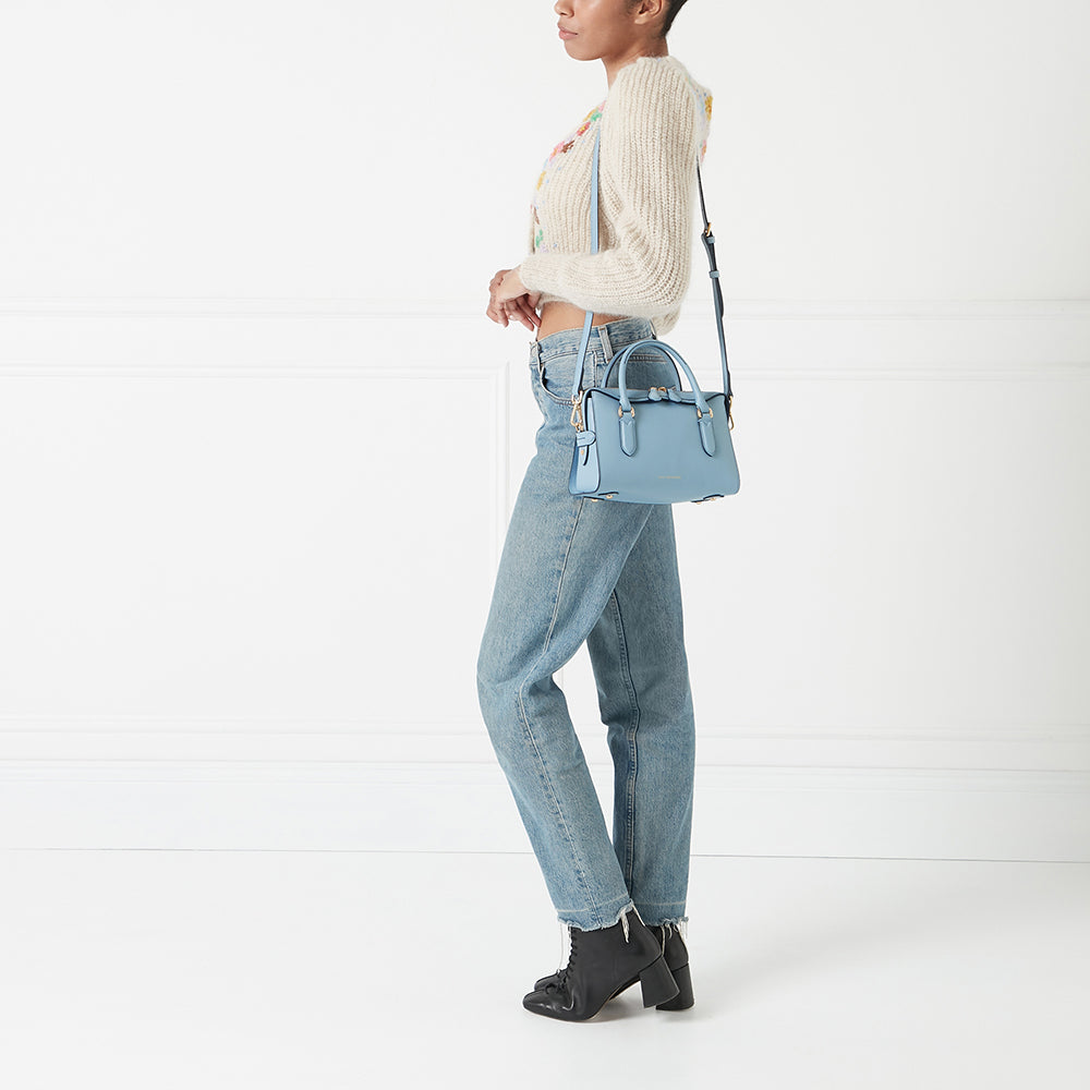 A pale blue satchel handbag worn by a model against a white background.
