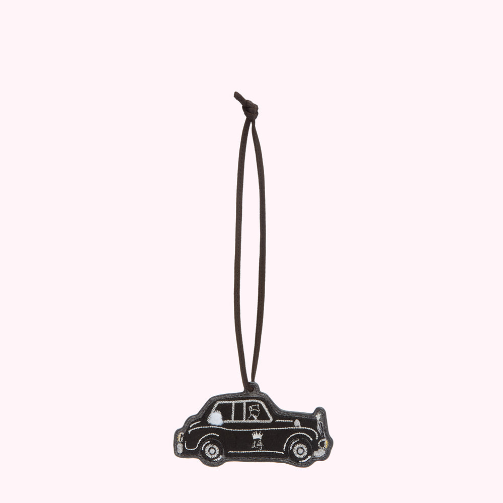 Black leather luggage tag shaped like a London cab, hanging from a brown cord.