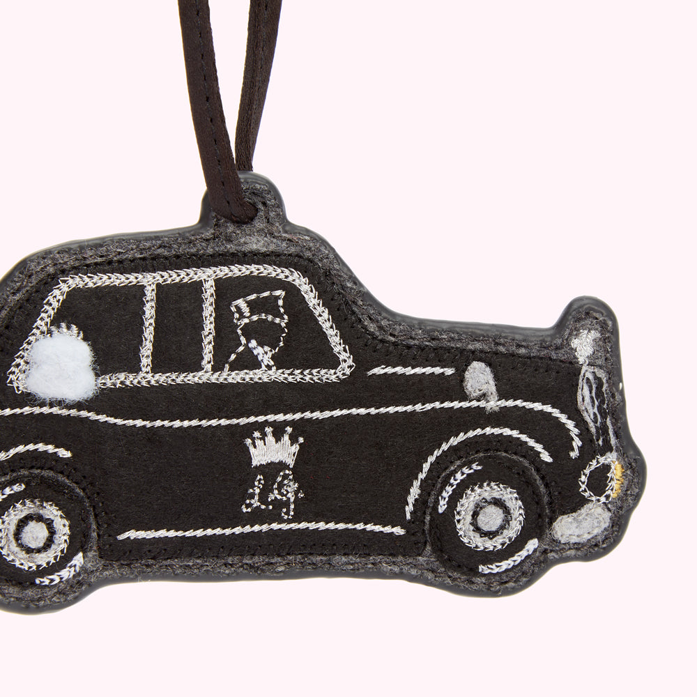 Black felt London taxi cab ornament with silver embroidered details, hanging from a brown cord.
