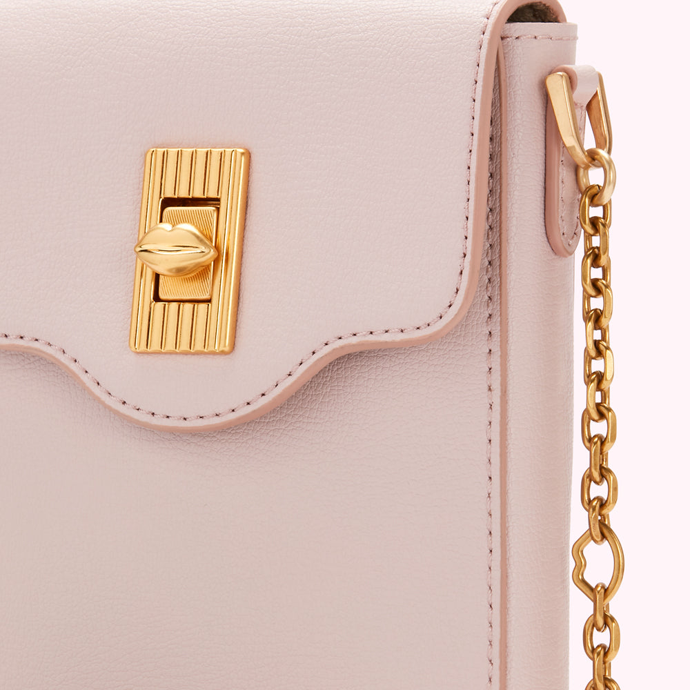 Close-up of a pale pink leather handbag with a gold lip-shaped clasp and gold chain strap.
