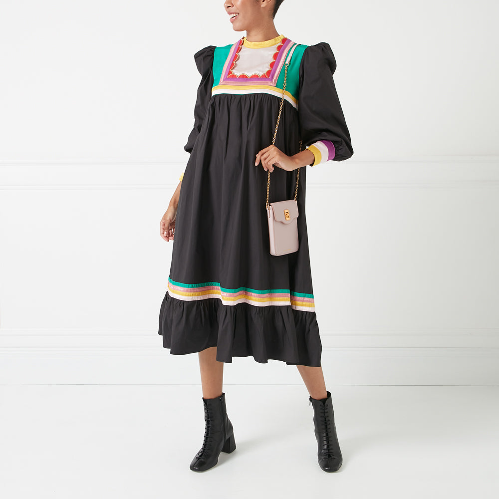 A model wearing a black midi dress with colorful embroidered details and a light pink crossbody bag against a white background.
