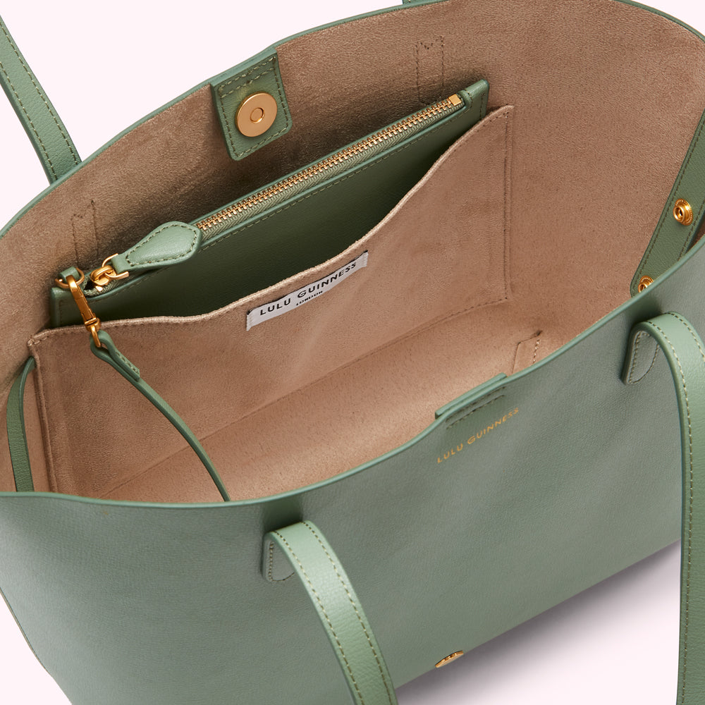 Sage green Lulu Guinness tote bag viewed from above, showcasing the interior's beige lining, zippered pocket, and branded label.
