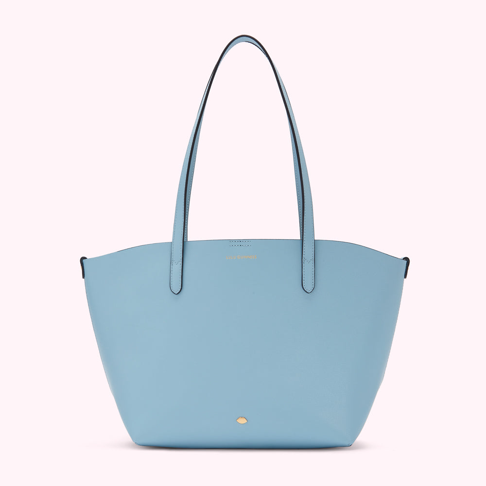 Light blue tote bag with black straps and small gold logo.
