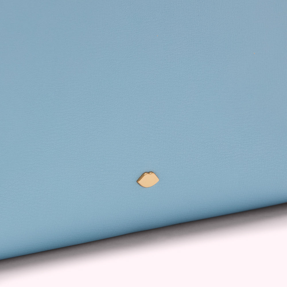 Close-up of a light blue leather surface with a small gold lip-shaped logo.
