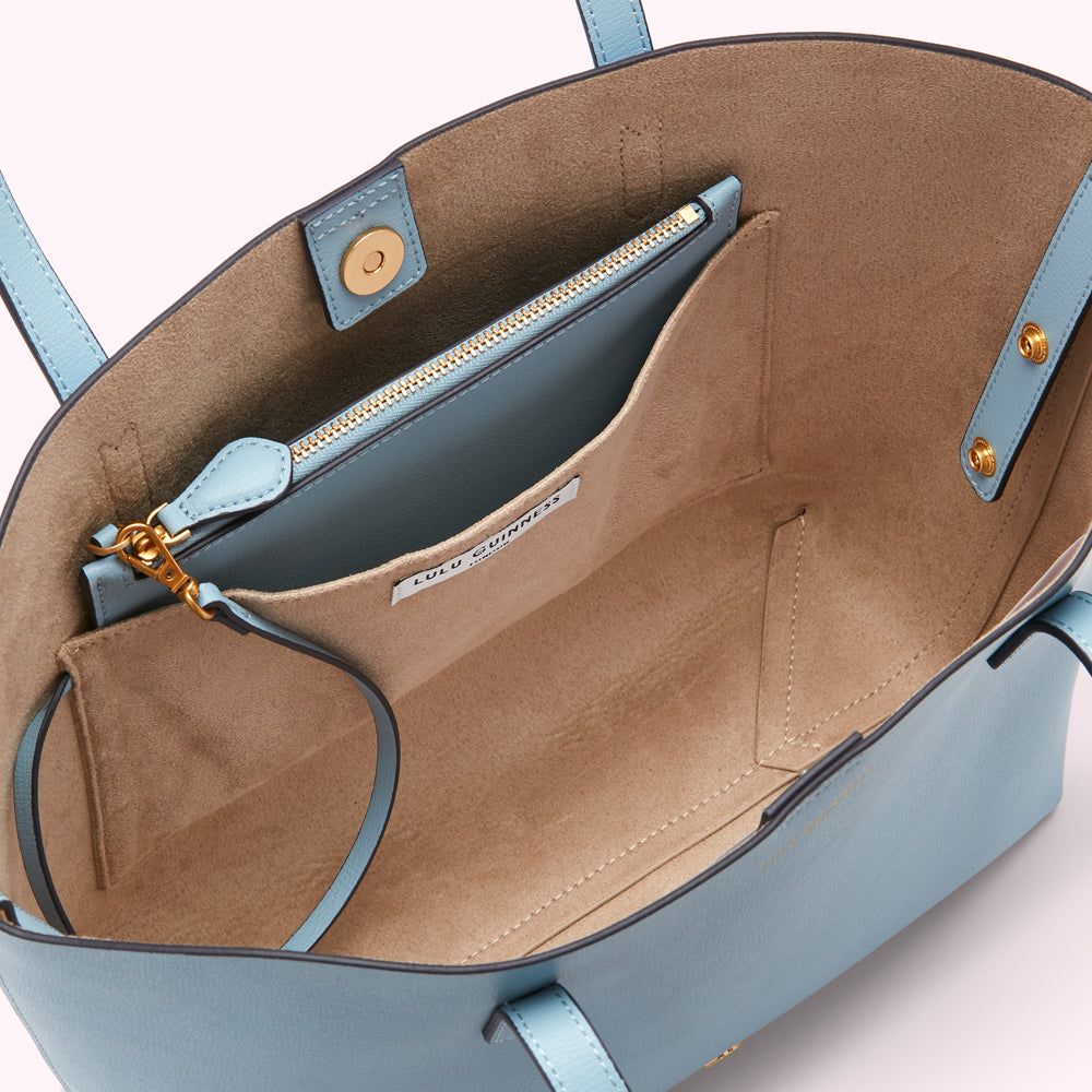 Interior view of a light blue Lulu Guinness tote bag, showing beige lining, zippered pocket, and brand label.
