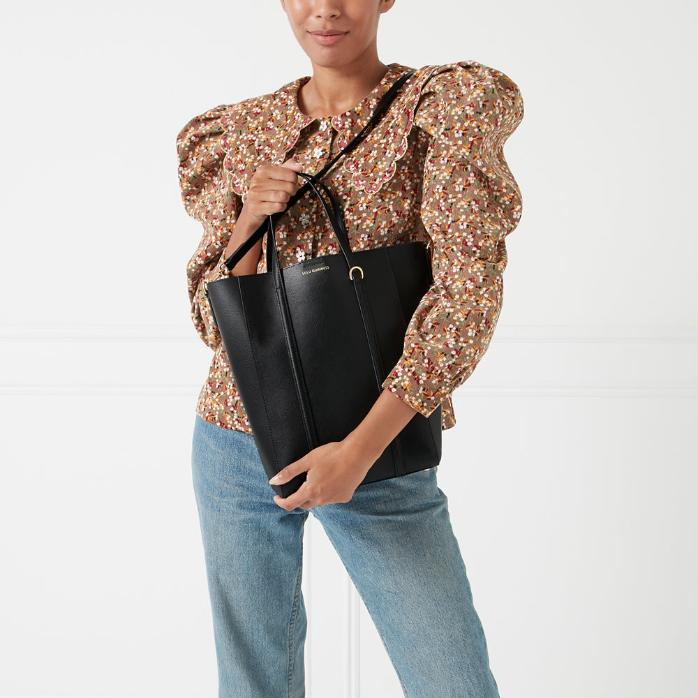 Woman holding a black Lulu Guinness tote bag against a white background.