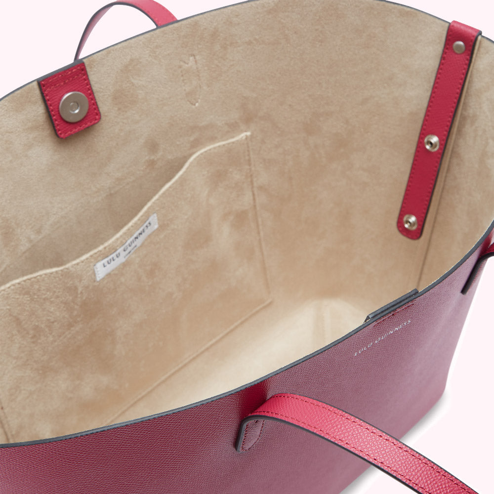 Inside of a crimson Lulu Guinness tote bag showing its beige interior and a small internal pocket.