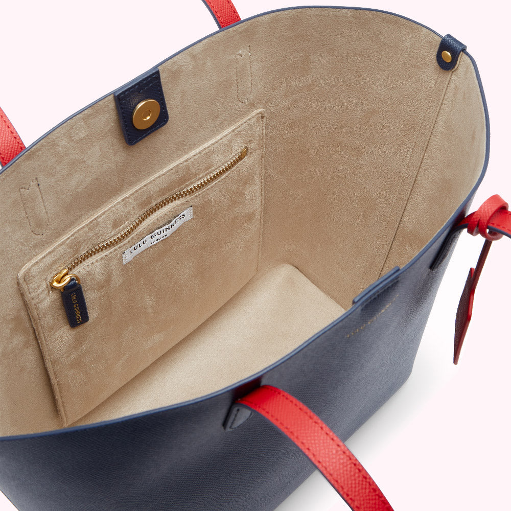 Inside of a navy blue Lulu Guinness tote bag with a beige interior and red accents on the straps.