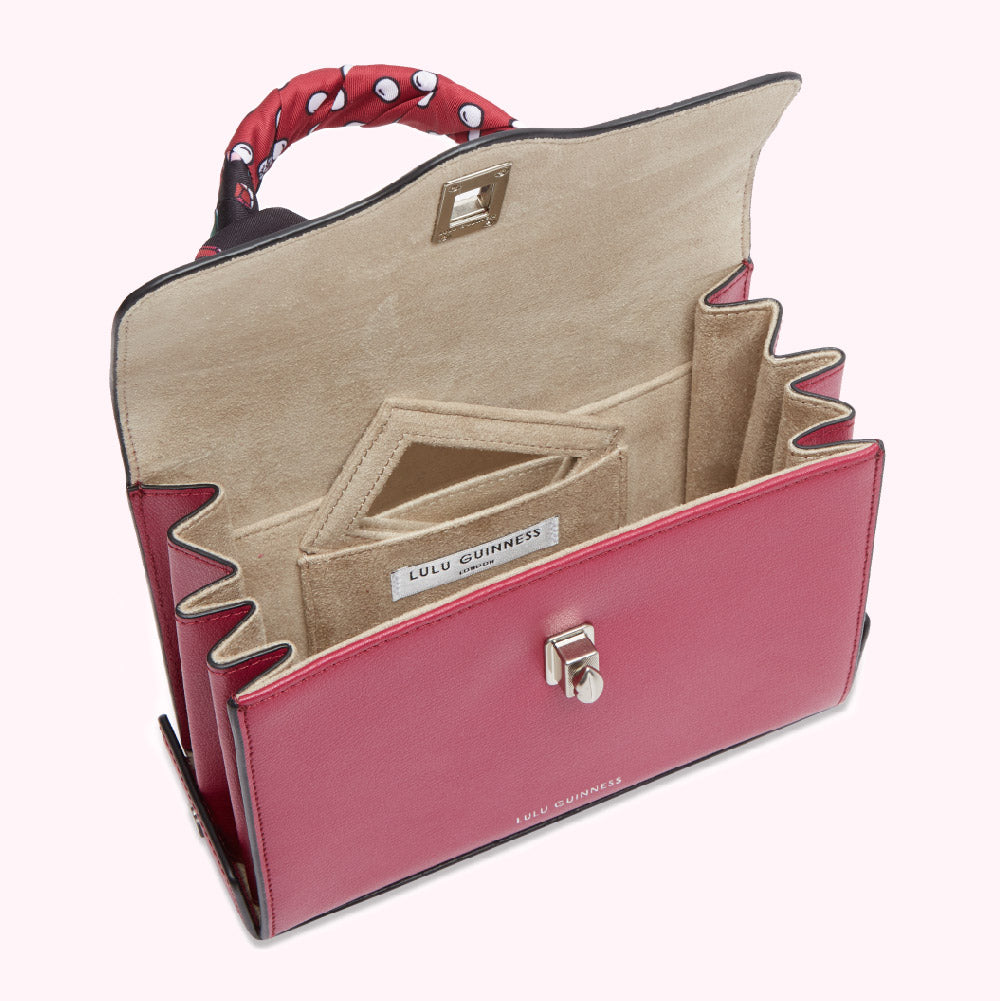 Open pink Lulu Guinness handbag with beige interior and patterned scarf handle.