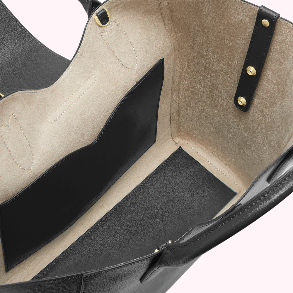 Inside of a black leather tote bag showing beige lining and interior pockets.