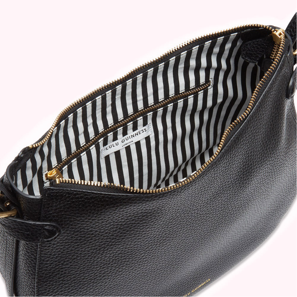 Black Lulu Guinness crossbody bag open to reveal its black and white striped interior.
