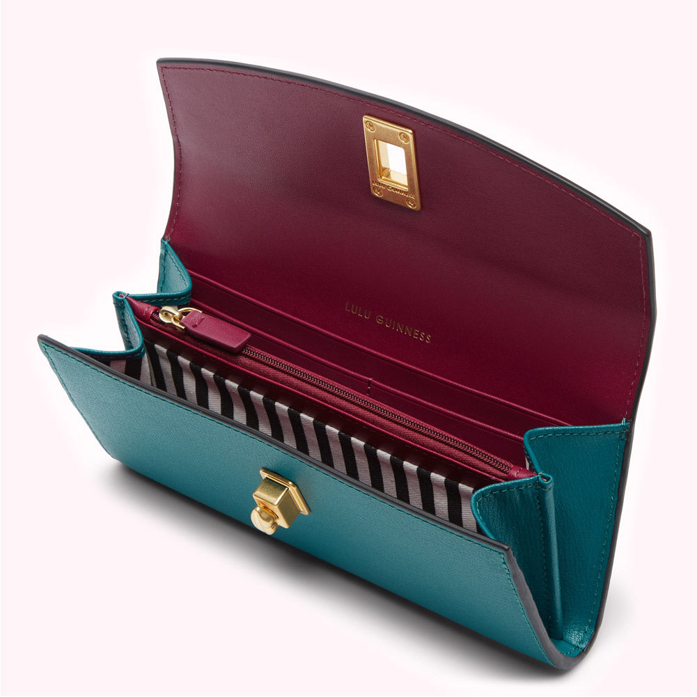 Open teal and burgundy Lulu Guinness wallet with gold hardware and black and white striped interior.
