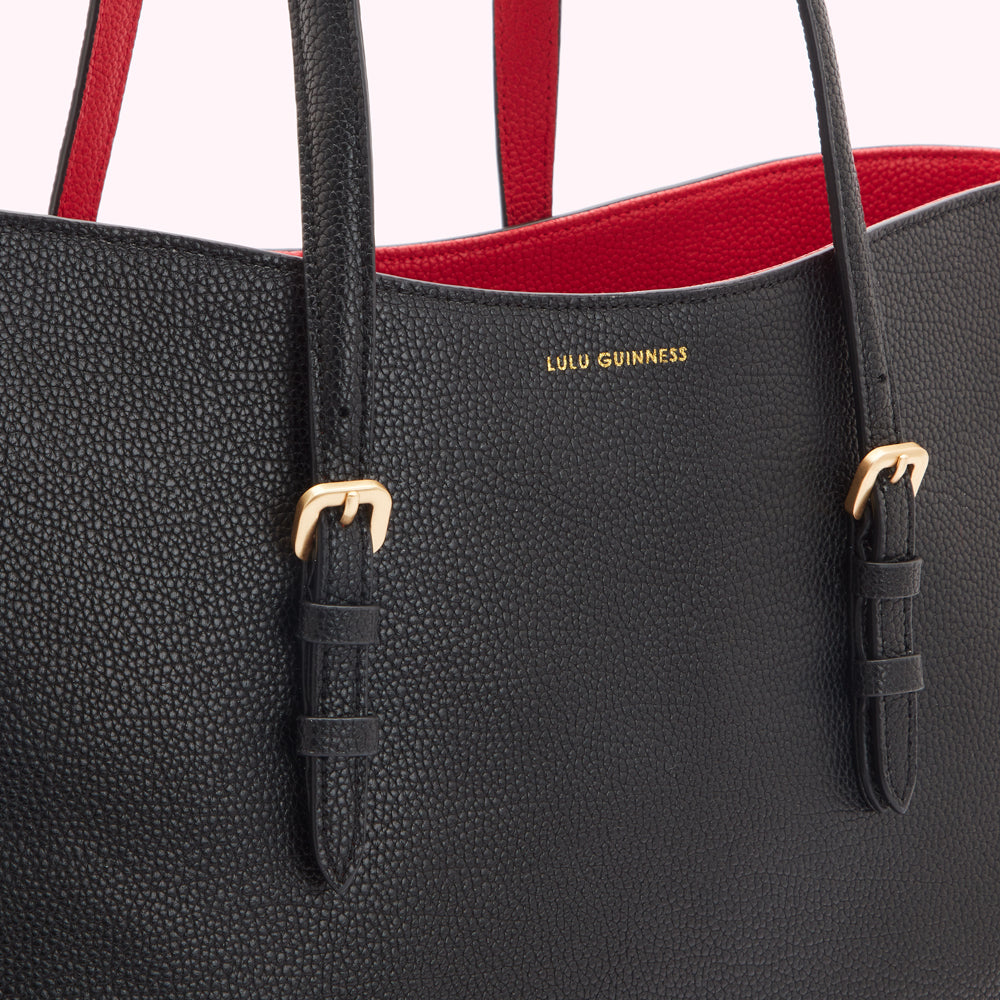 Close-up of a black Lulu Guinness tote bag with red interior and gold buckles.
