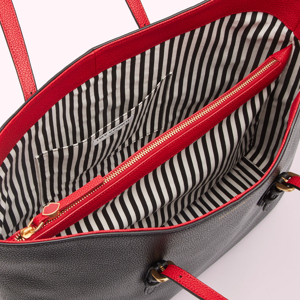 Interior of a black Lulu Guinness tote bag with red trim and a black and white striped lining.