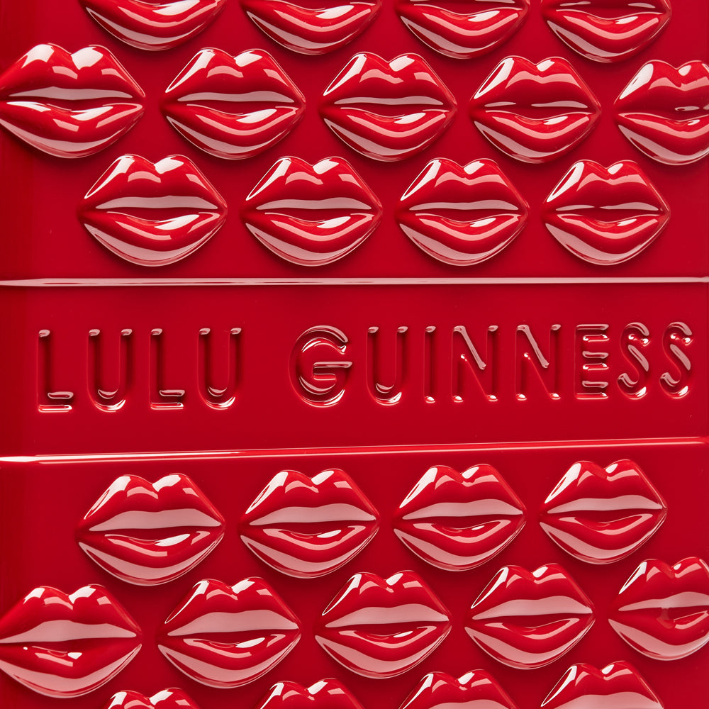 Close-up of a red Lulu Guinness product featuring a repeating pattern of red lips and the brand name embossed on the surface.