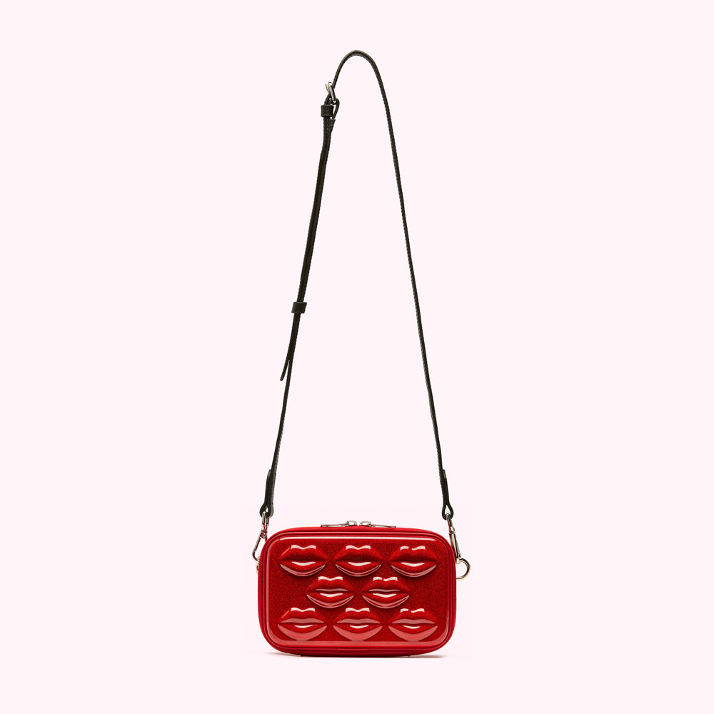 Red crossbody bag with lip-shaped embellishments and a black strap against a white background.
