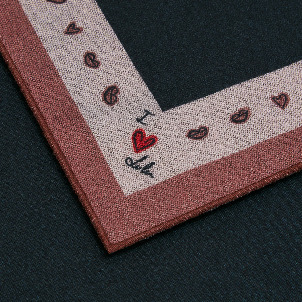 Close-up of a dark-colored textile with a pink and beige border featuring a repeating pattern of hearts and coffee beans, and the text "I love".