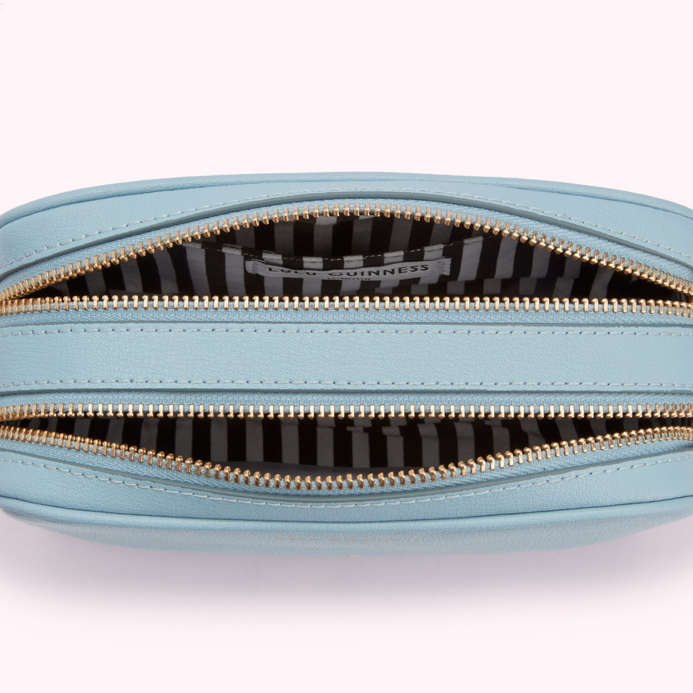 Close-up view of a light blue Lulu Guinness double zip pouch open to reveal a black and white striped interior.

