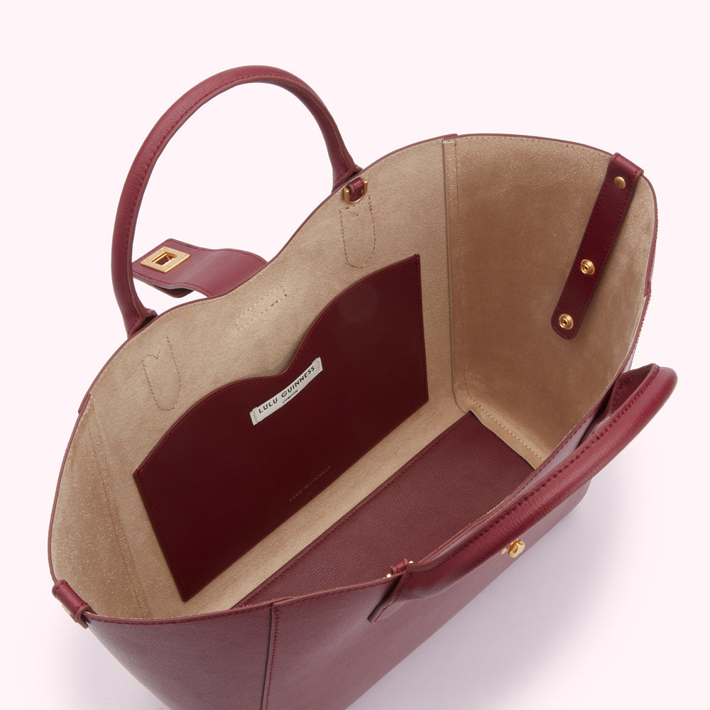 Inside view of a burgundy Lulu Guinness tote bag, showcasing the beige interior, internal pocket, and gold-tone hardware.
