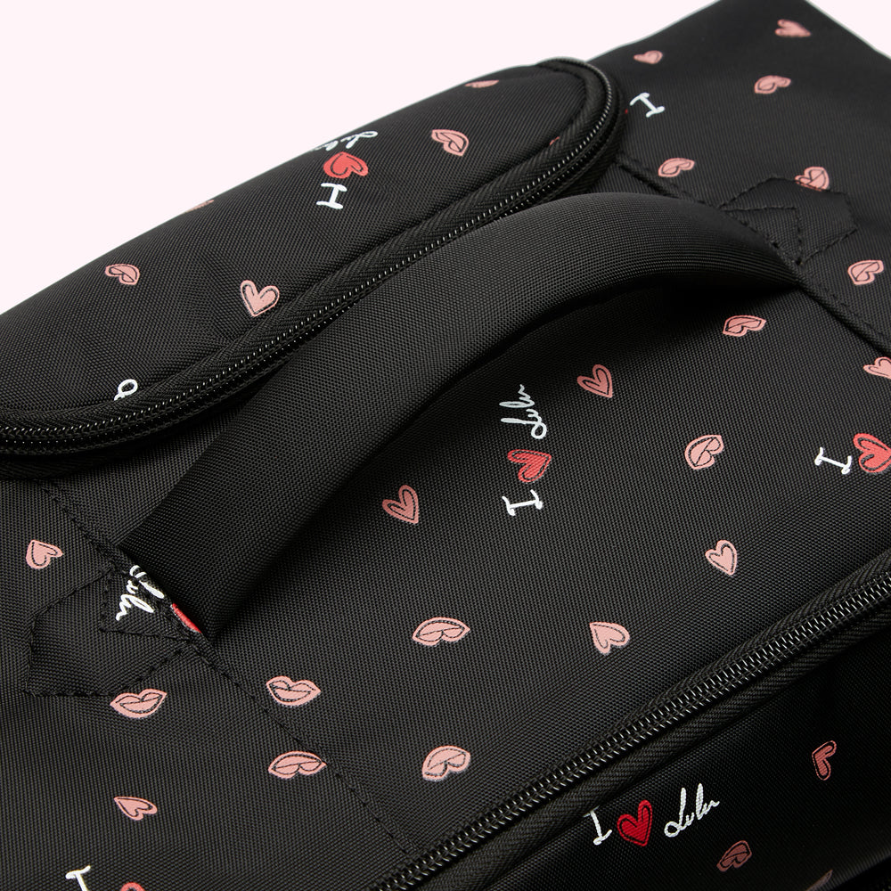 Close-up of a black backpack with a pink and white "I love lulu" pattern and a top handle.
