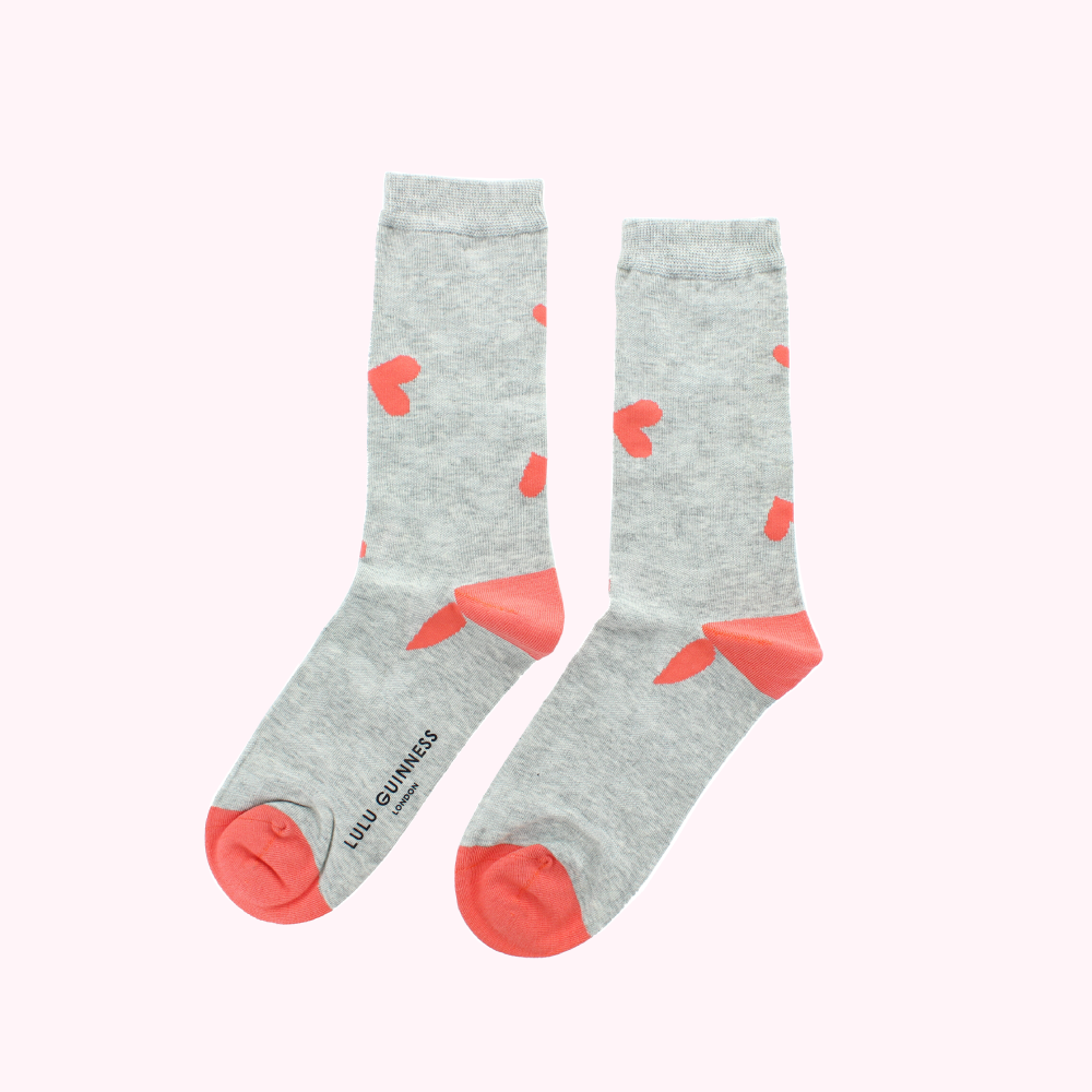 Pair of grey socks with coral hearts and a coral heel and toe. Lulu Guinness London is printed on the sole of one sock.