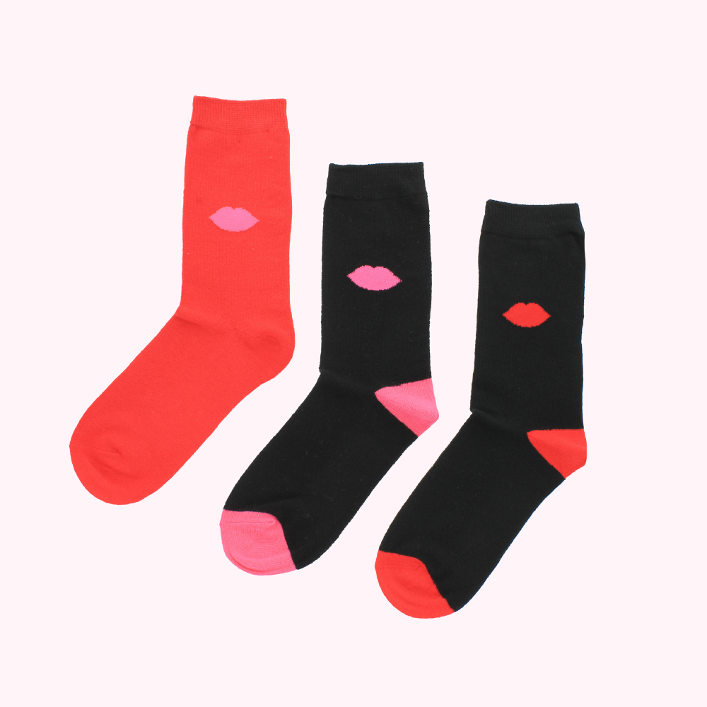 Three pairs of socks with lip print designs; one pair is red with pink lips, one pair is black with pink lips and the other pair is black with red lips.
