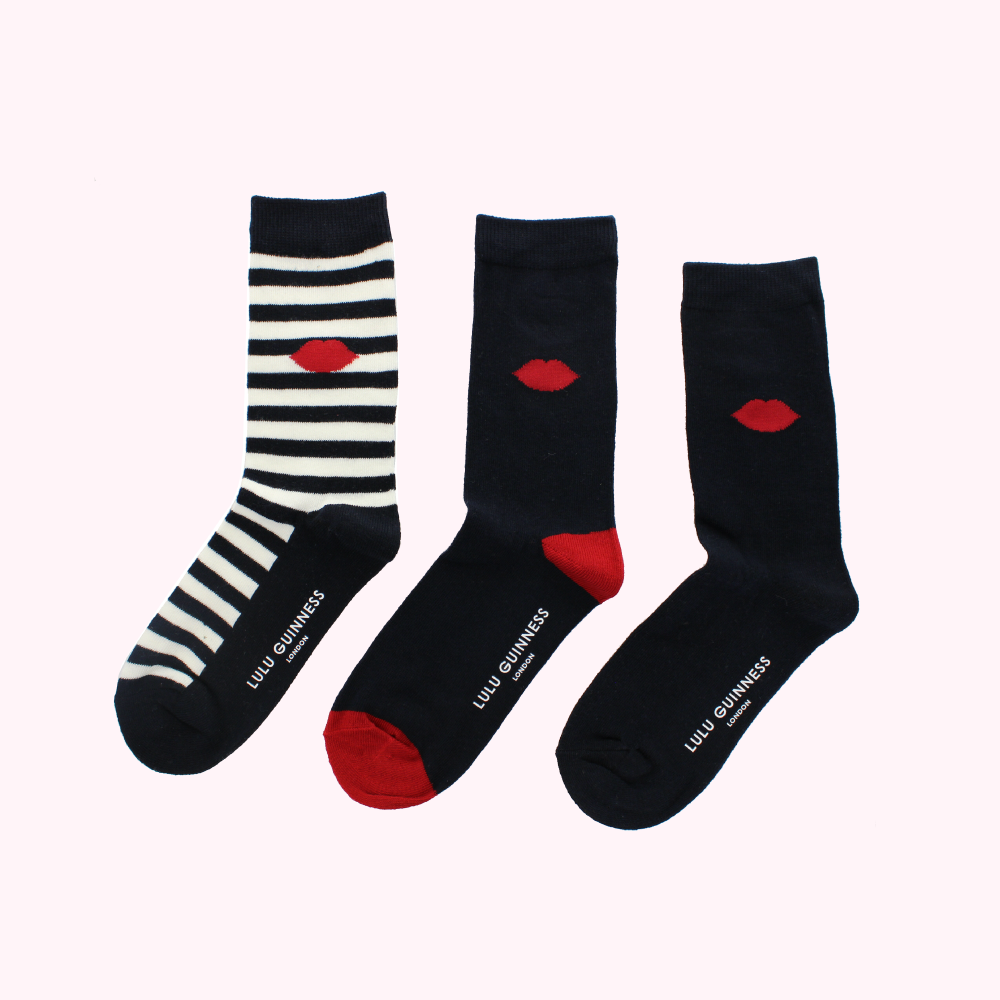 Three pairs of Lulu Guinness socks against a white background. One pair is navy blue with red lips, one pair is black and white striped with red lips, and one pair is navy blue with red lips.